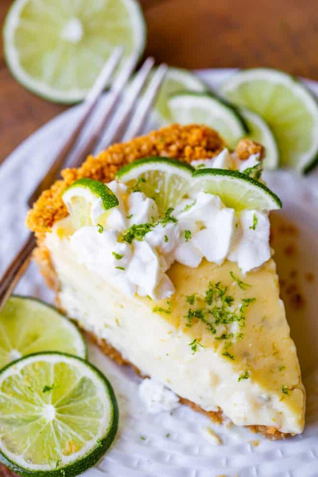 Μια φέτα Key lime pie με σαντιγί και φέτες λάιμ σε ένα πιάτο με ένα πιρούνι.