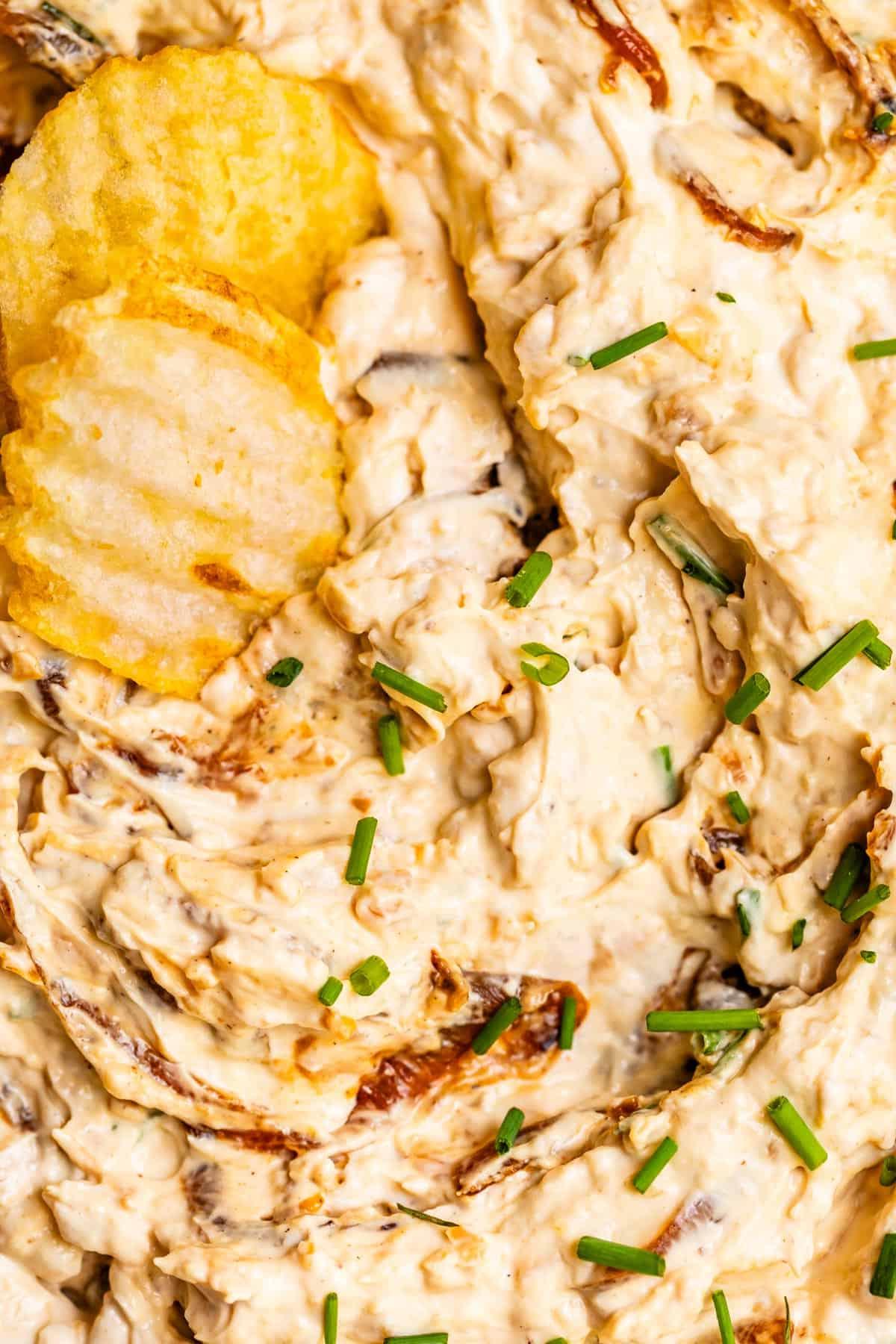 Δύο κυματιστά πατατάκια φωλιασμένα σε French Onion Dip με γαρνιτούρα σχοινόπρασου.