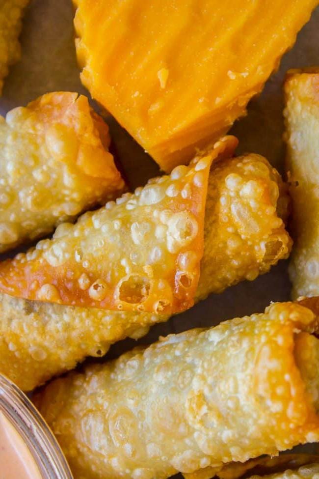 Τυρομπέργκερ Ρολά Αυγού από το The Food Charlatan. Πρόκειται για έναν από τους καλύτερους συνδυασμούς όλων των εποχών! Εννοώ, γέμιση κιμά με τυρί τηγανισμένη σε φύλλα; Πώς μπορεί να πάει κάτι στραβά εδώ; Βουτήξτε τα σε μια υπέροχη σάλτσα τηγανίσματος και θα βρεθείτε στον παράδεισο του τυρομπέργκερ σε χρόνο μηδέν! #τυρομπέργκερ #μπέργκερ #κιμάς #τυρί #τηγανητό #βαθύτηγανισμένο #εύκολο #συνταγή #μοσχάρι #σπιτικό #πώς_να_φτιάξεις #σάλτσα_τηγανίσματος #ορεκτικό #ντιπ Τυρομπέργκερ ρολά αυγού κοντά σε ένα κομμάτι τυρί τσένταρ.