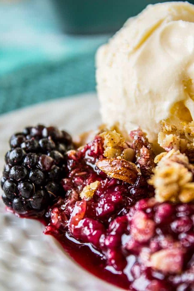 Εύκολη Συνταγή Cobbler με Βατόμουρα με Επικάλυψη Τραγανής Βρώμης από το The Food Charlatan. Αυτή η συνταγή για Cobbler με βατόμουρα είναι τόσο εύκολη που είναι απίστευτη! Η τραγανή επικάλυψη βρώμης ετοιμάζεται εξαιρετικά γρήγορα και είναι το τέλειο συμπλήρωμα στην καλύτερη προσφορά του καλοκαιριού: τα βατόμουρα. #cobbler #blackberries #easy #oats #dessert #summerrecipes #homemade #summer #crisp Κοντινό πλάνο cobbler με βατόμουρα με παγωτό και φρέσκα βατόμουρα σε πιάτο.