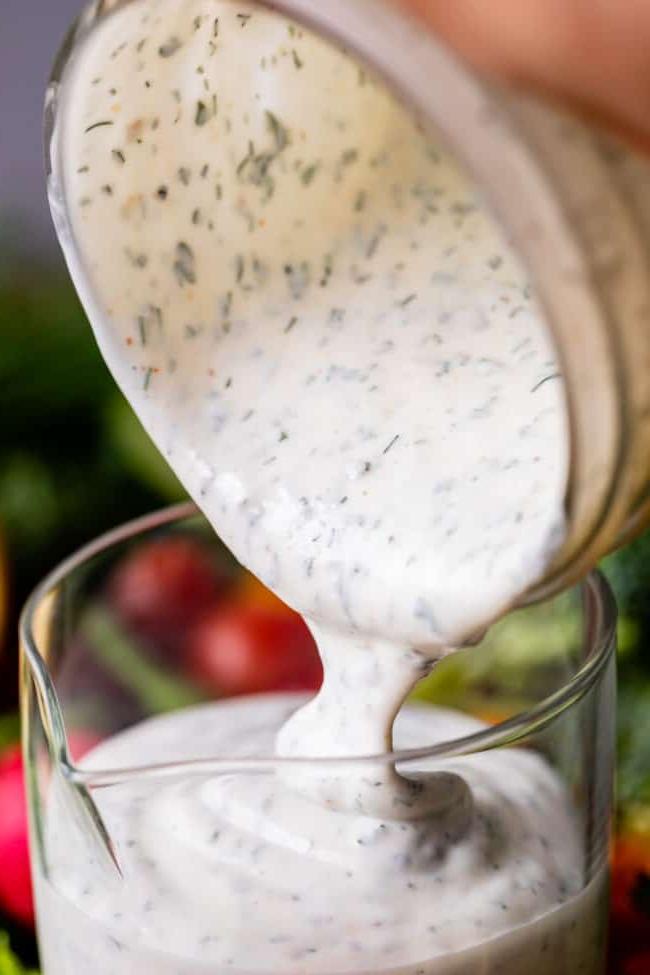 Κρεμώδης Σως Ranch με Βουτυρόγαλα από το The Food Charlatan. Το μόνο πράγμα που είναι καλύτερο από την έτοιμη σως ranch εστιατορίου είναι η Σπιτική Σως Ranch με Βουτυρόγαλα! Είναι τόσο ονειρεμένη, κρεμώδης και η συνταγή είναι απίστευτα εύκολη. Θα σας δείξω πώς ακριβώς να την φτιάξετε! Ετοιμαστείτε για την καλύτερη σαλάτα της ζωής σας! #ranch #dip #easy #recipe #salad #healthy #buttermilk #sourcream #freshherbs #dried #spices #homemade #fromscratch #restaurant #diy #howtomake Κρεμώδης συνταγή σως ranch με βουτυρόγαλα χύνεται από γυάλινο βάζο σε γυάλινη μεζούρα.