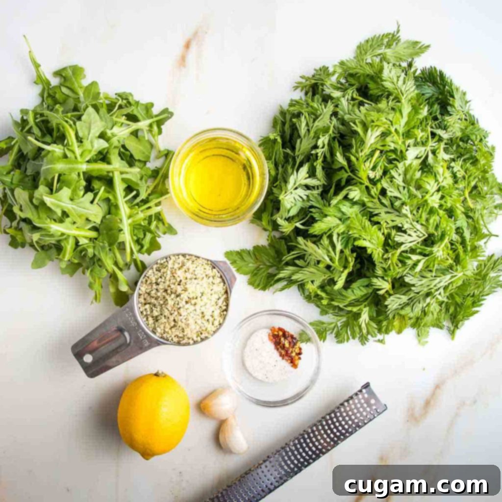 A curated selection of ingredients for carrot greens pesto: fresh carrot greens, arugula, hemp seeds, a whole lemon, garlic cloves, and a small bowl of spices and olive oil.