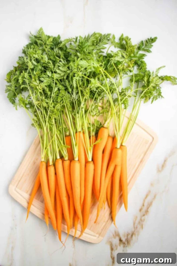 A bunch of fresh carrots with their long, leafy greens still attached, laid on a wooden cutting board, ready for preparation.