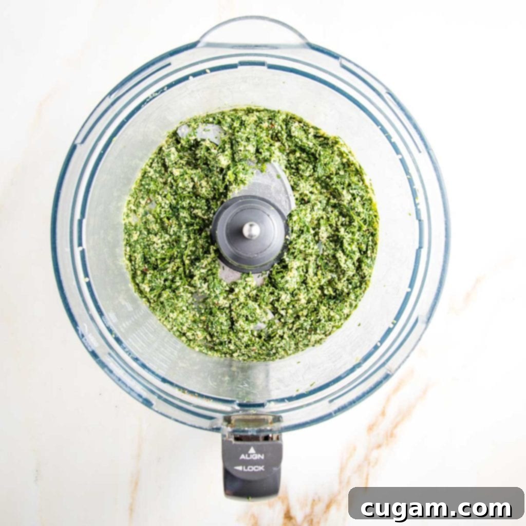 A food processor bowl containing vibrant, bright green pesto, which has been processed to a chunky consistency.