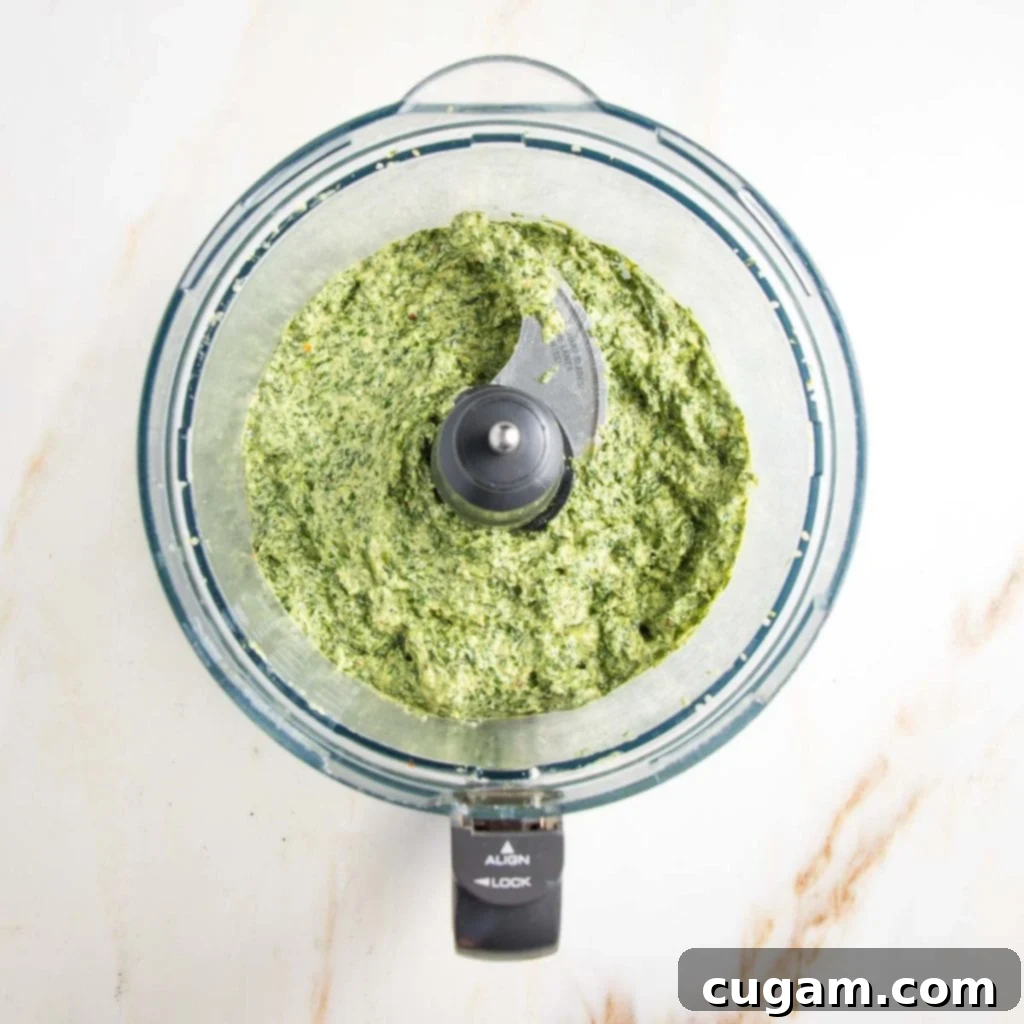 Creamy, bright green pesto in the bowl of a food processor after the olive oil has been streamed in and emulsified.