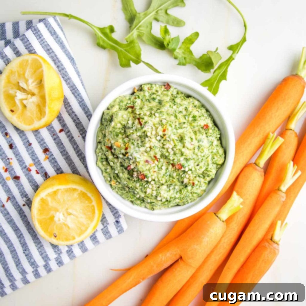 A beautifully arranged setting with fresh carrots, lemons, and arugula surrounding a bowl of vibrant carrot top pesto, ready to be served.