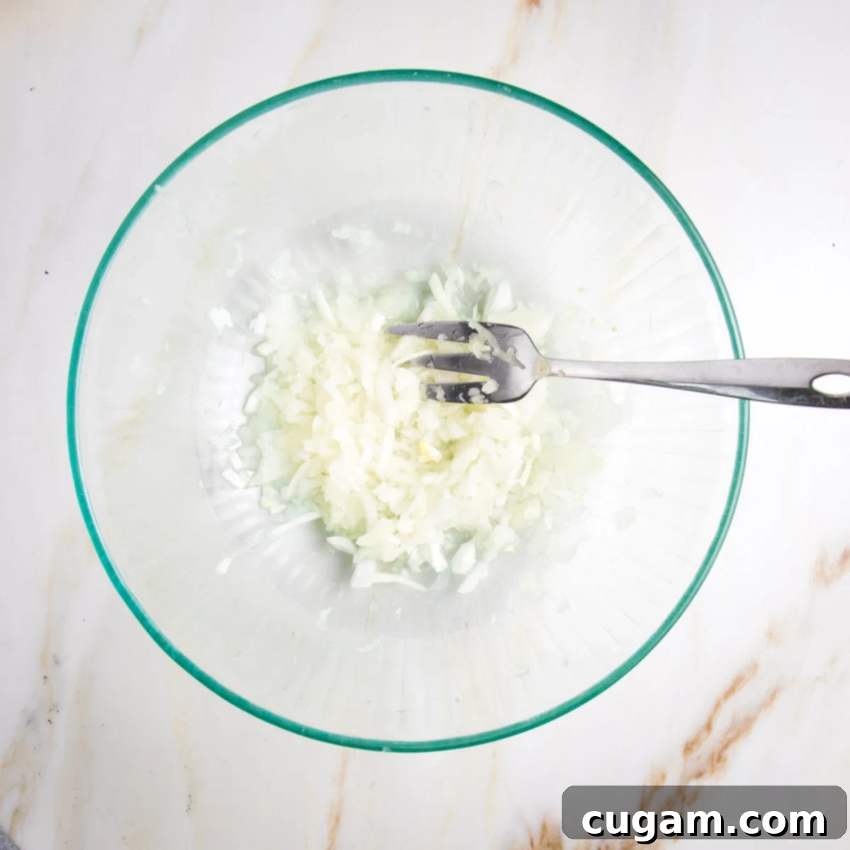 Shredded white onions and juices in a glass bowl.