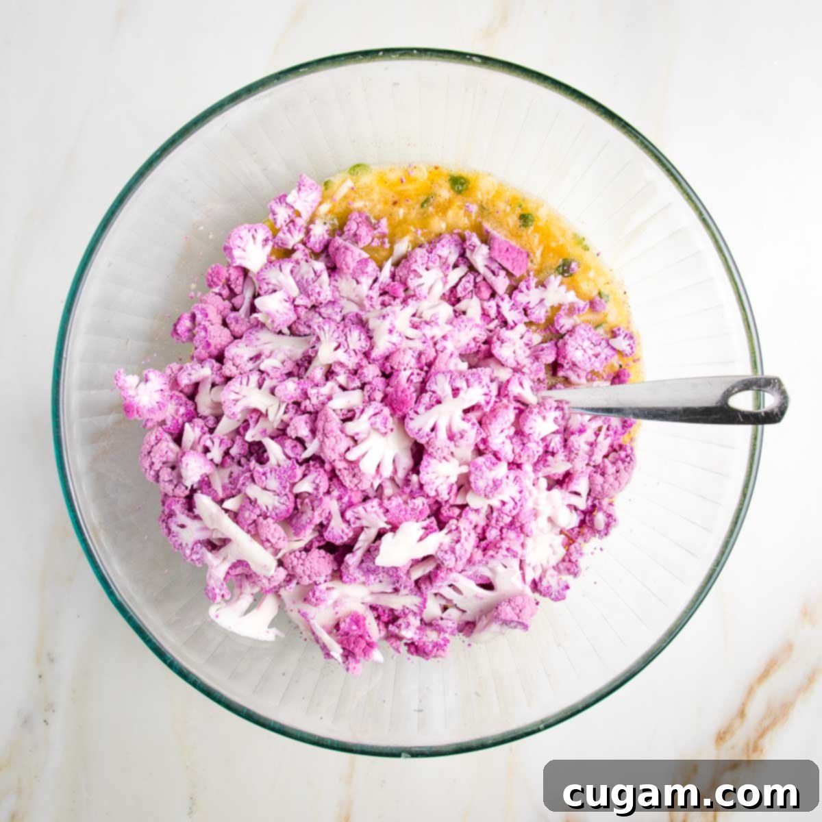 Whisked eggs and spices in a glass bowl, with small pieces of purple cauliflower on top