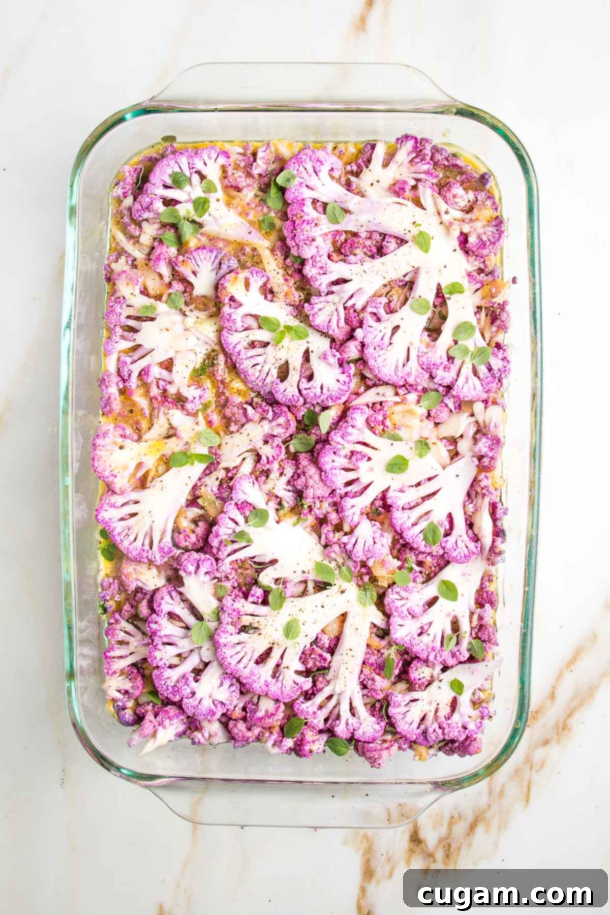 Purple cauliflower thinly sliced and placed on the top of a casserole dish filled with cauliflower kugel, ready to bake.