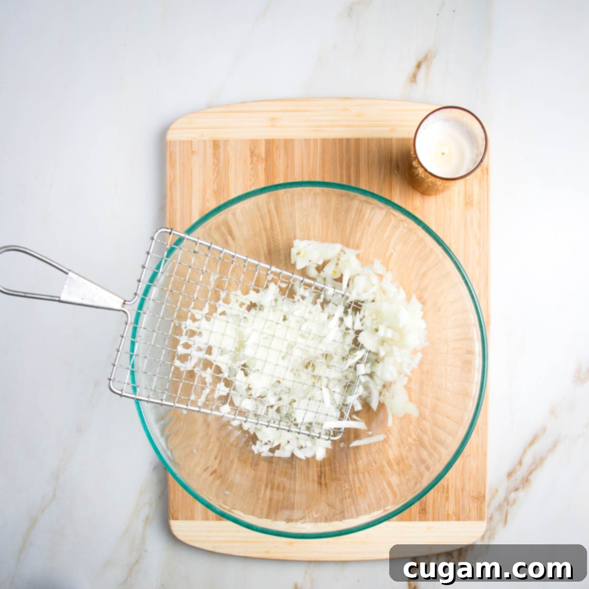 Close up of an onion being shredded over a glass bowl, with a lit candle nearby.