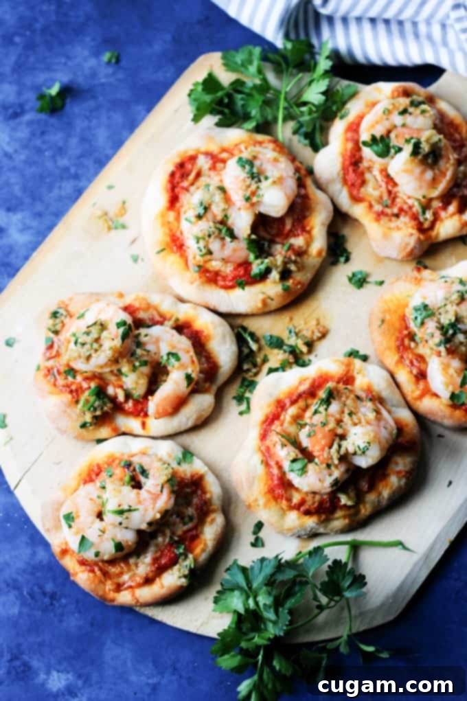 A vibrant pizzette with garlic shrimp, roasted red pepper pesto, and Mahon-Menorca cheese on a pizza peel, ready to be enjoyed.