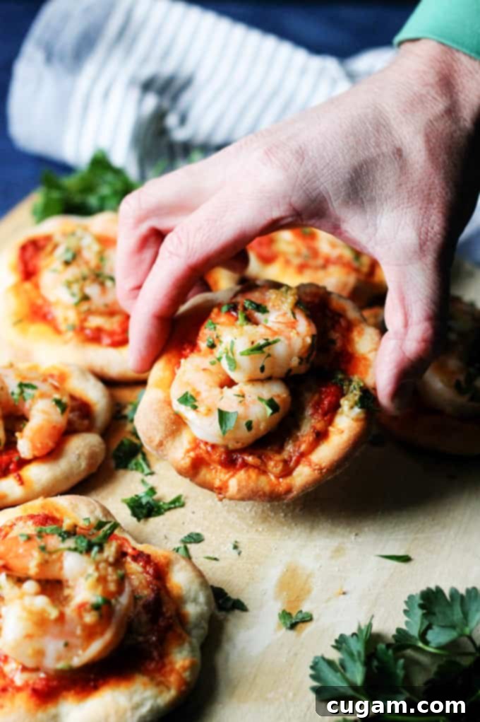 A single pizzette with garlic shrimp and roasted red pepper pesto being lifted from a pizza peel.