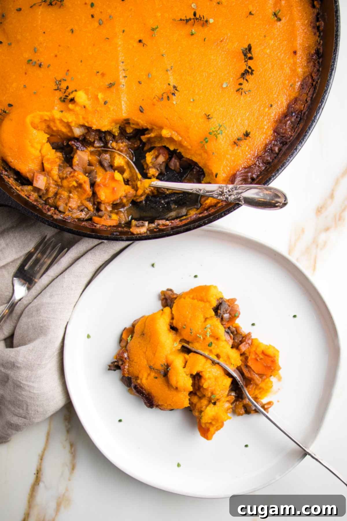 Cast iron skillet with cooked veggie shepherd's pie topped with sweet potato mash. A white rimmed plate is filled with a piece of shepherd's pie and a fork cutting through the middle. of it.
