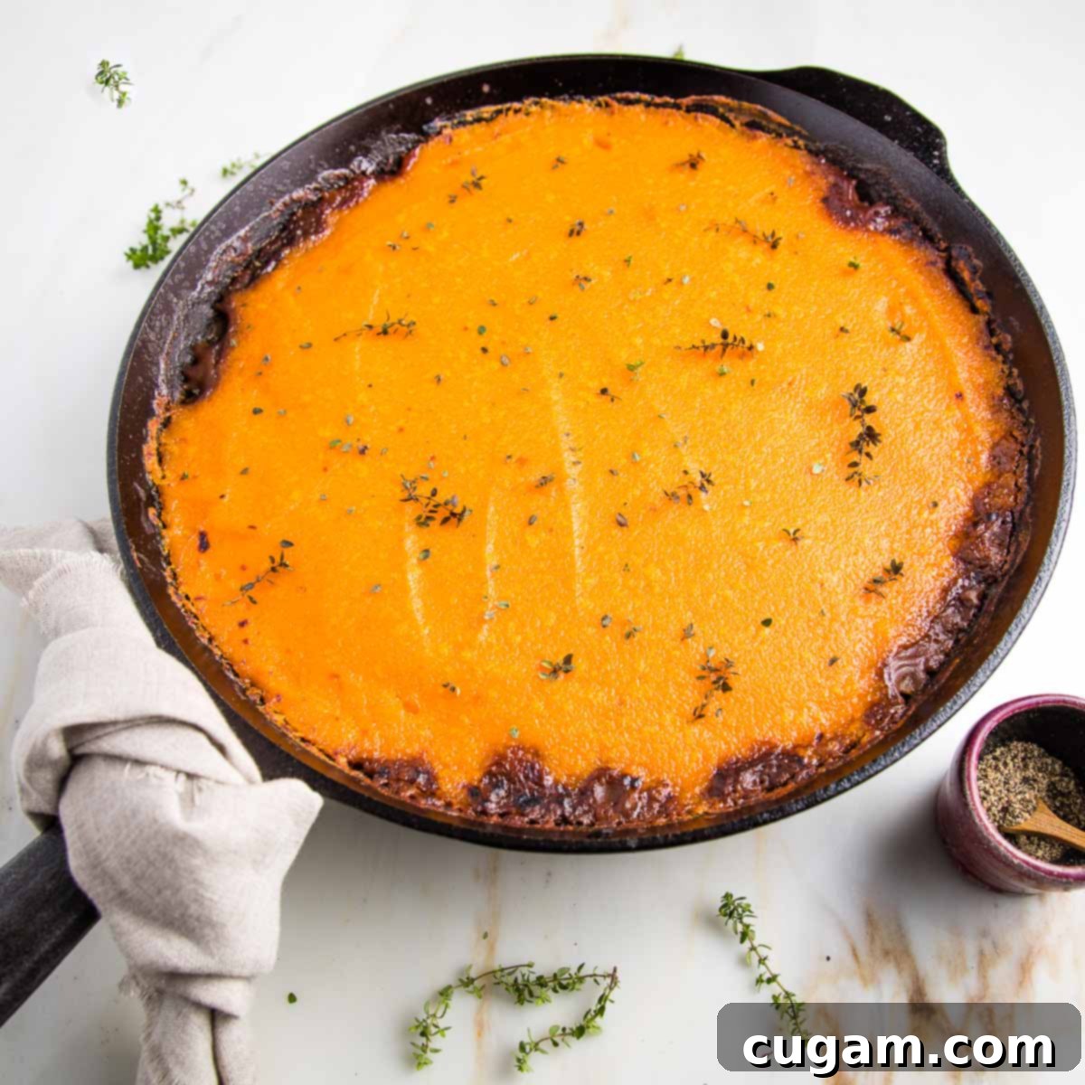 Cast iron skillet filled with vegan shepherd's pie that's topped with sweet potato mash and sprinkled with fresh thyme. 