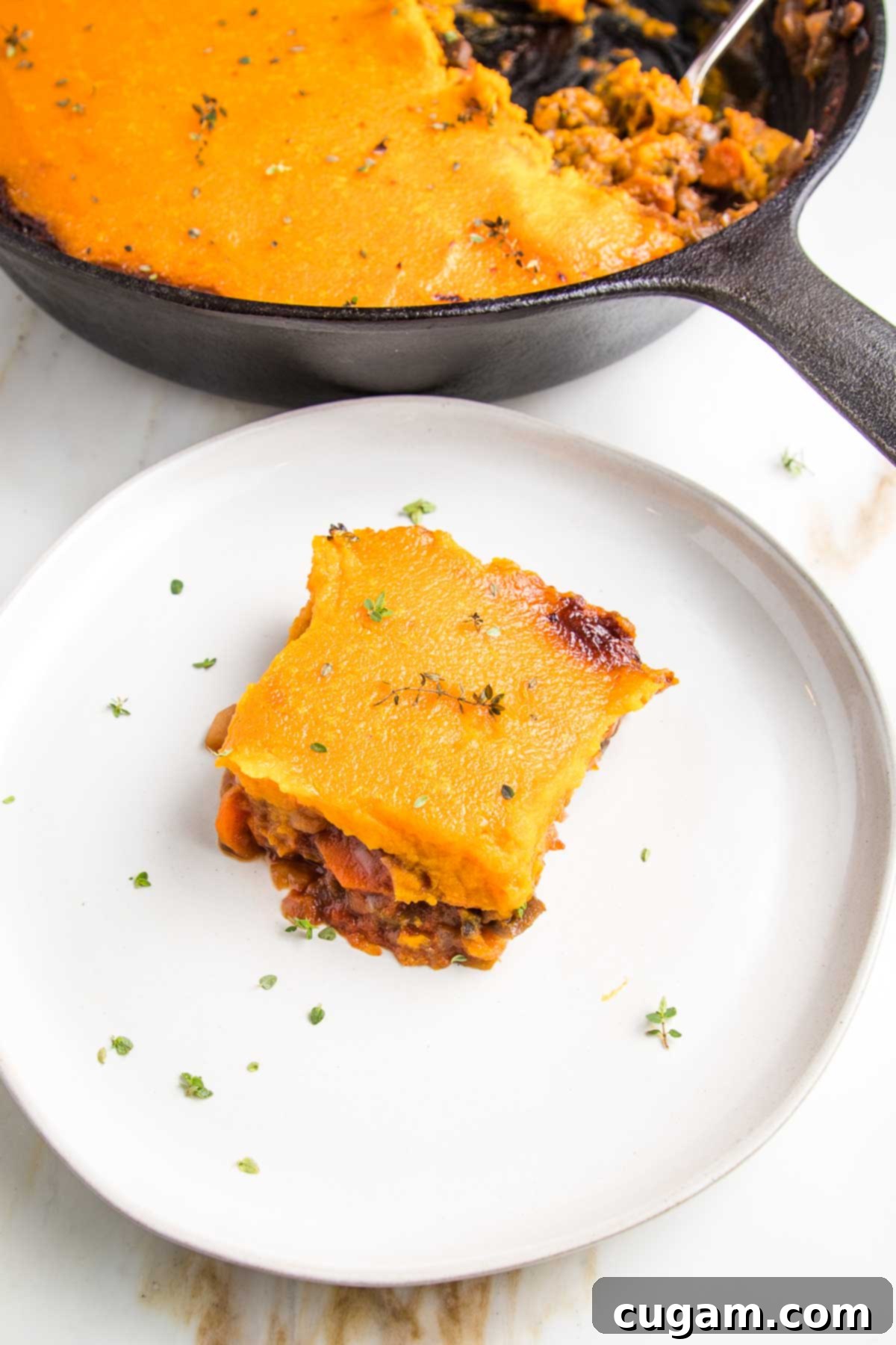 white rimmed plate with piece of shepherd's pie, topped with sweet potato mash. There's a skillet with veggie shepherd's pie in the background. 
