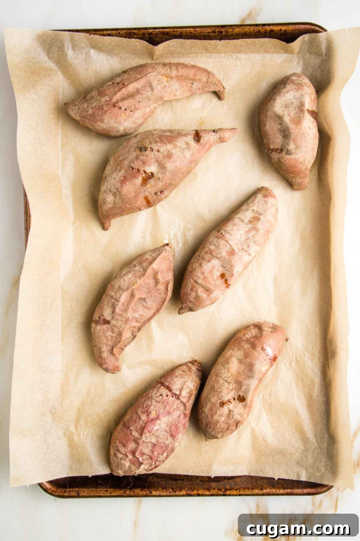 Shriveled baked sweet potatoes on a parchment lined baking sheet.