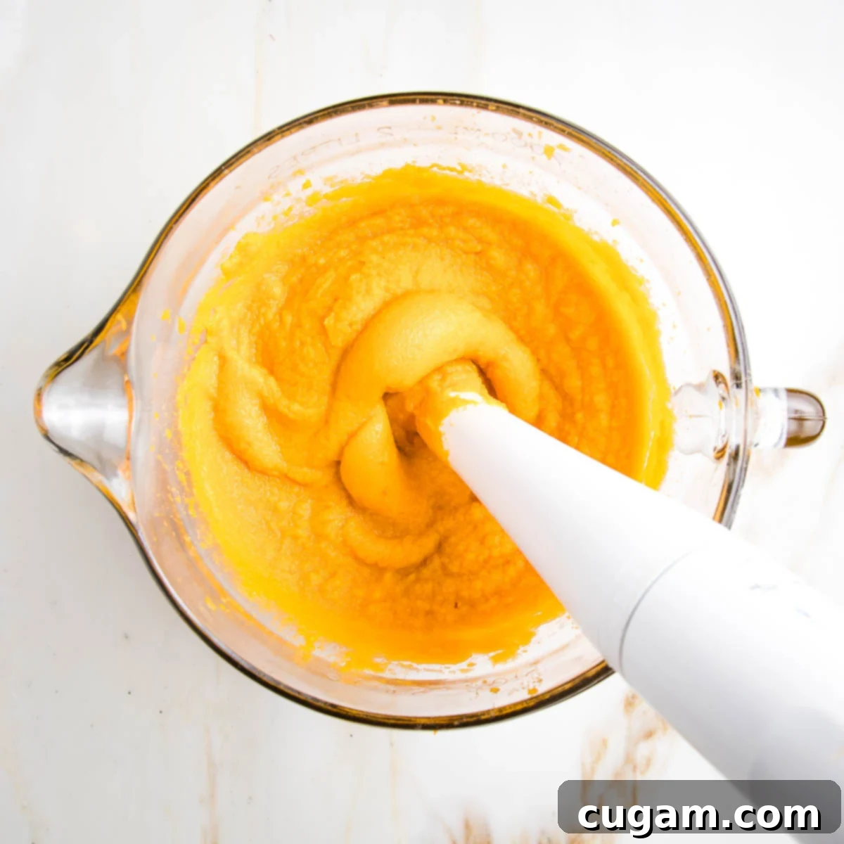 Immersion blender pureeing the bright orange flesh of cooked sweet potatoes.