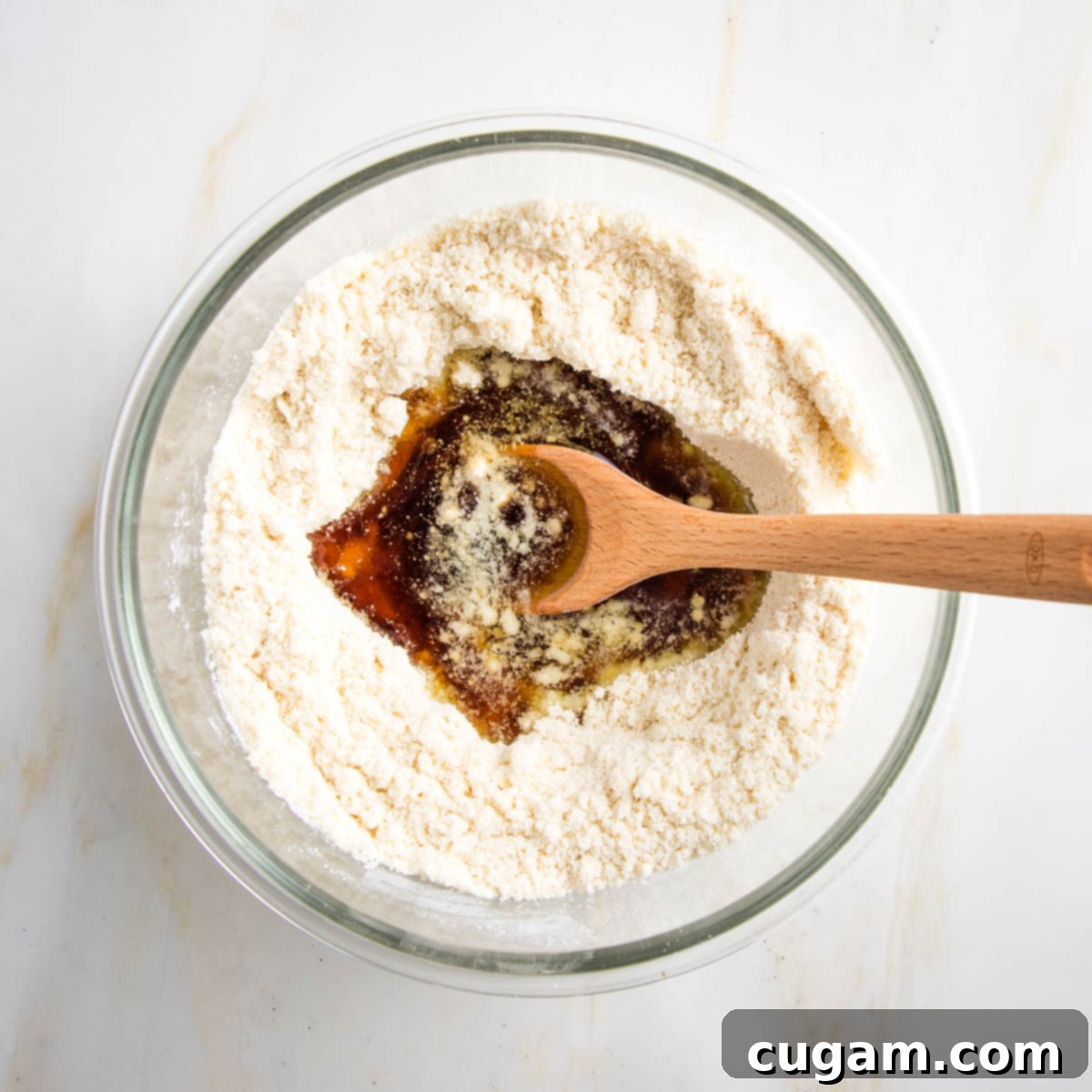 Dry ingredients in a large bowl, hole made in center and we ingredients poured into the hole. There is a wooden spoon in the bowl.