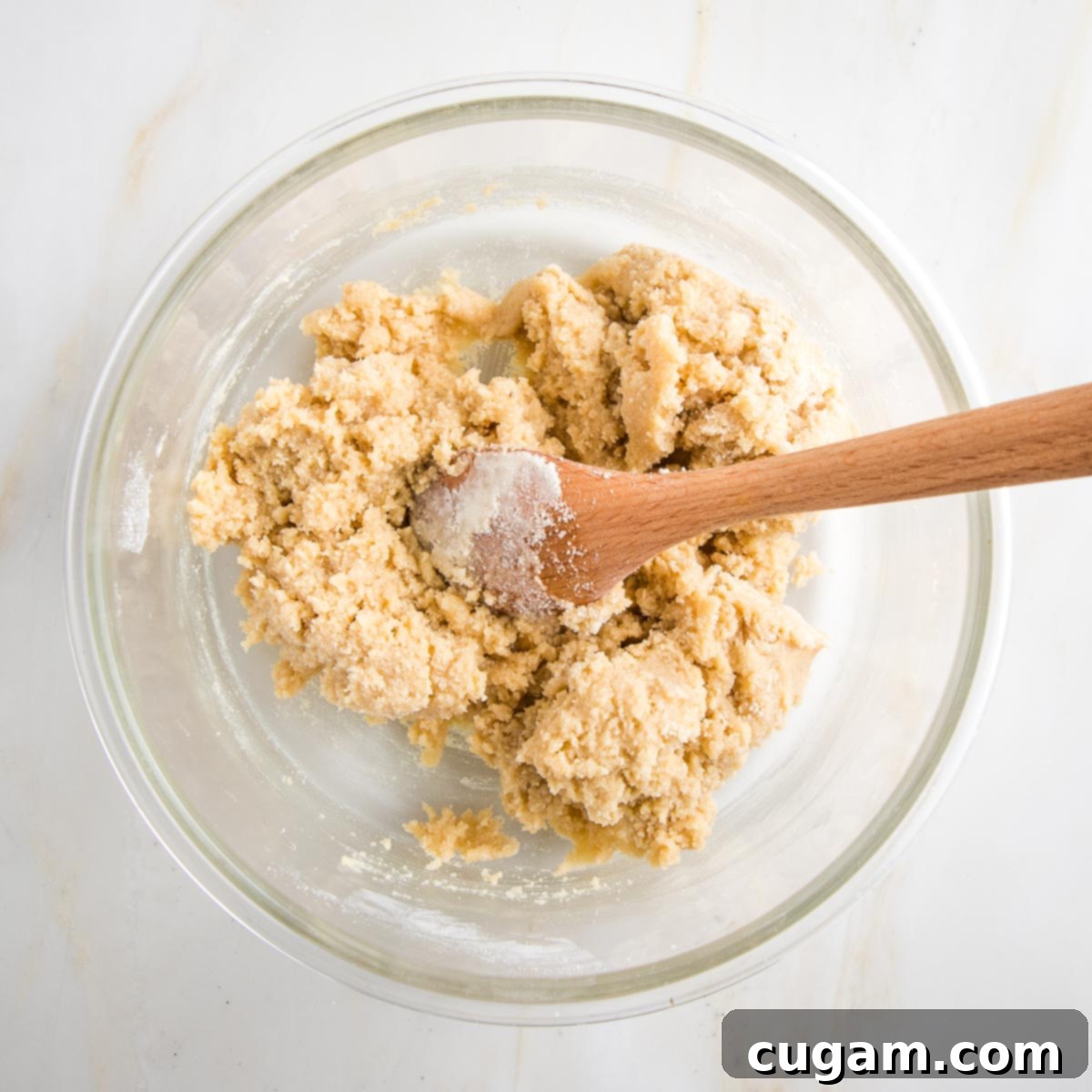 Large glass bowl with a wooden spoon that has mixed together biscotti dough.