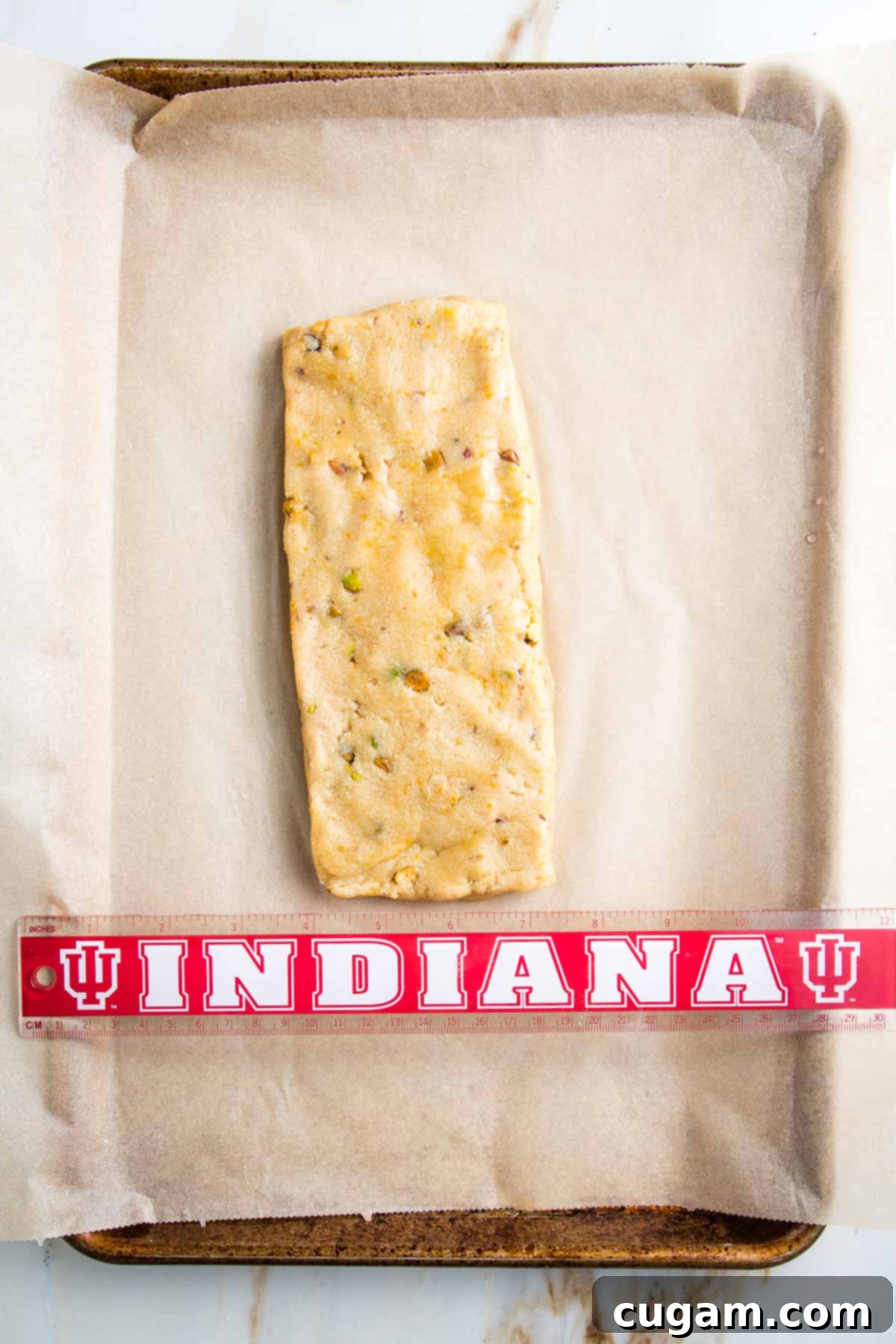 Biscotti dough log on a parchment lined baking tray with ruler underneath measuring 3.5" wide.