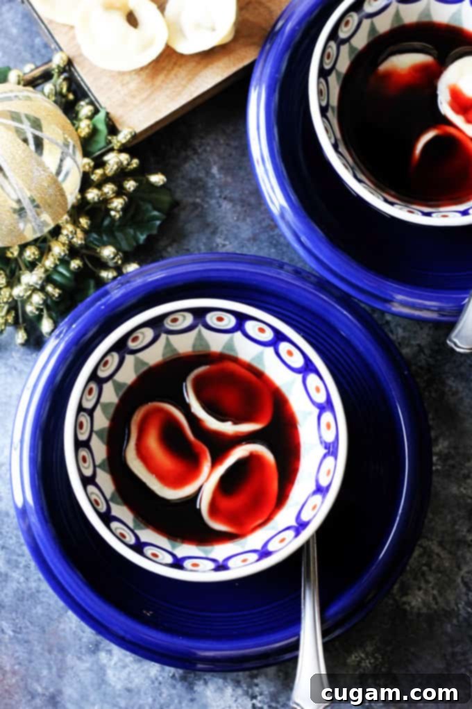 Two blue bowls filled with traditional Polish Borscht and mushroom pierogi Uszka, garnished with fresh herbs.