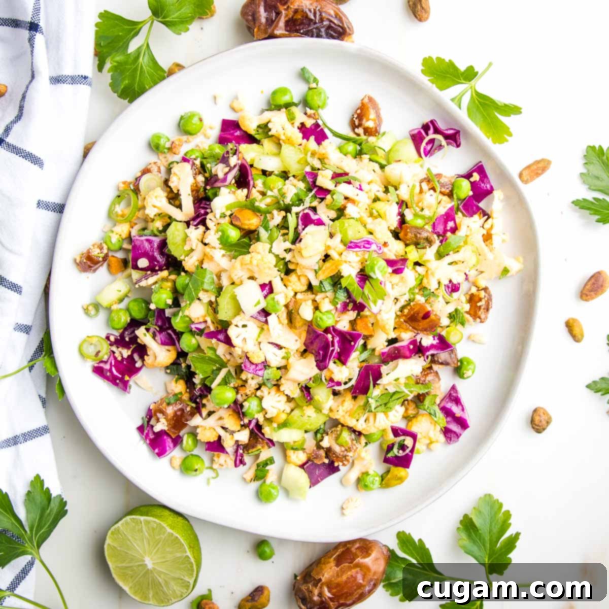 Chopped cauliflower, cabbage, dates and nuts on a round plate with limes and fresh herbs.