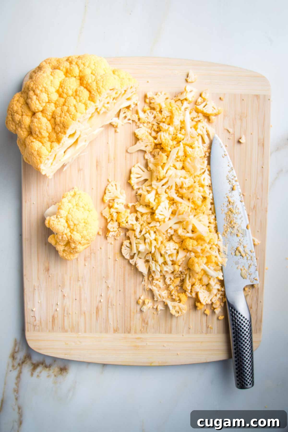 Wooden cutting board with head of yellow cauliflower. Half is already sliced super thin with a sharp knife.