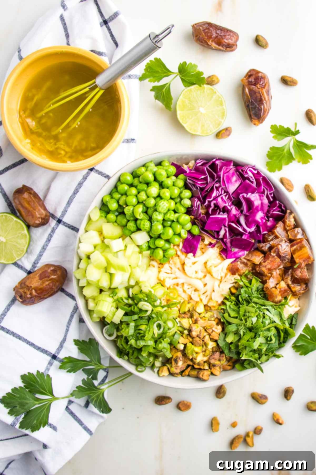 Salad in colorful sections of purple cabbage,green peas, yellow cauliflower, green scallions, brown dates with a small bowl lime vinaigrette, dates, lime and fresh herbs