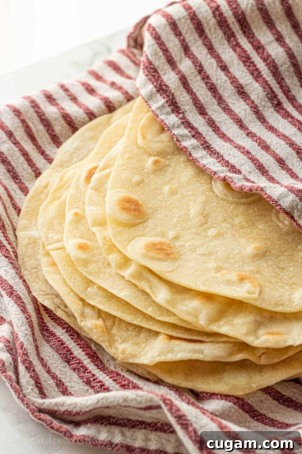 Stack of freshly cooked sourdough discard tortillas wrapped in a red dish towel, ready to be served.