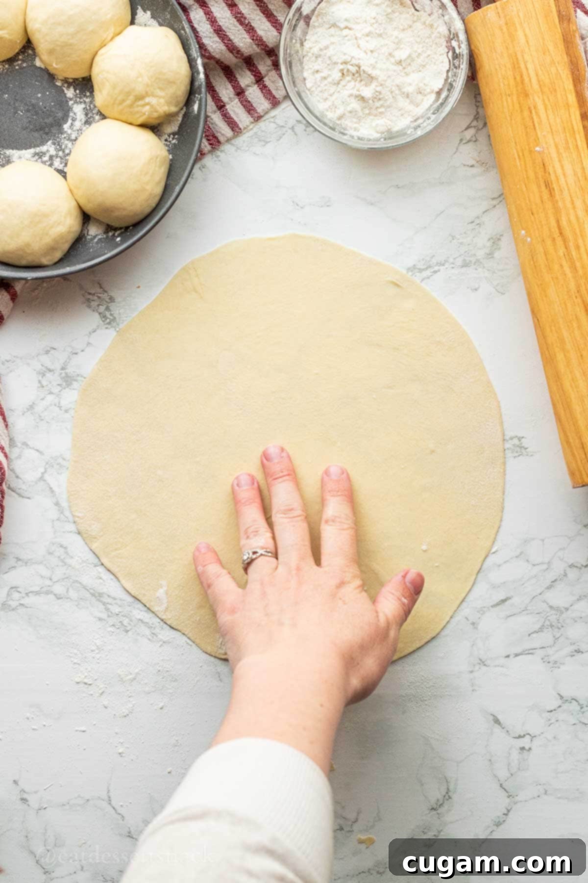 A thin, flat sourdough discard tortilla being rolled out on a floured countertop with a wooden rolling pin.