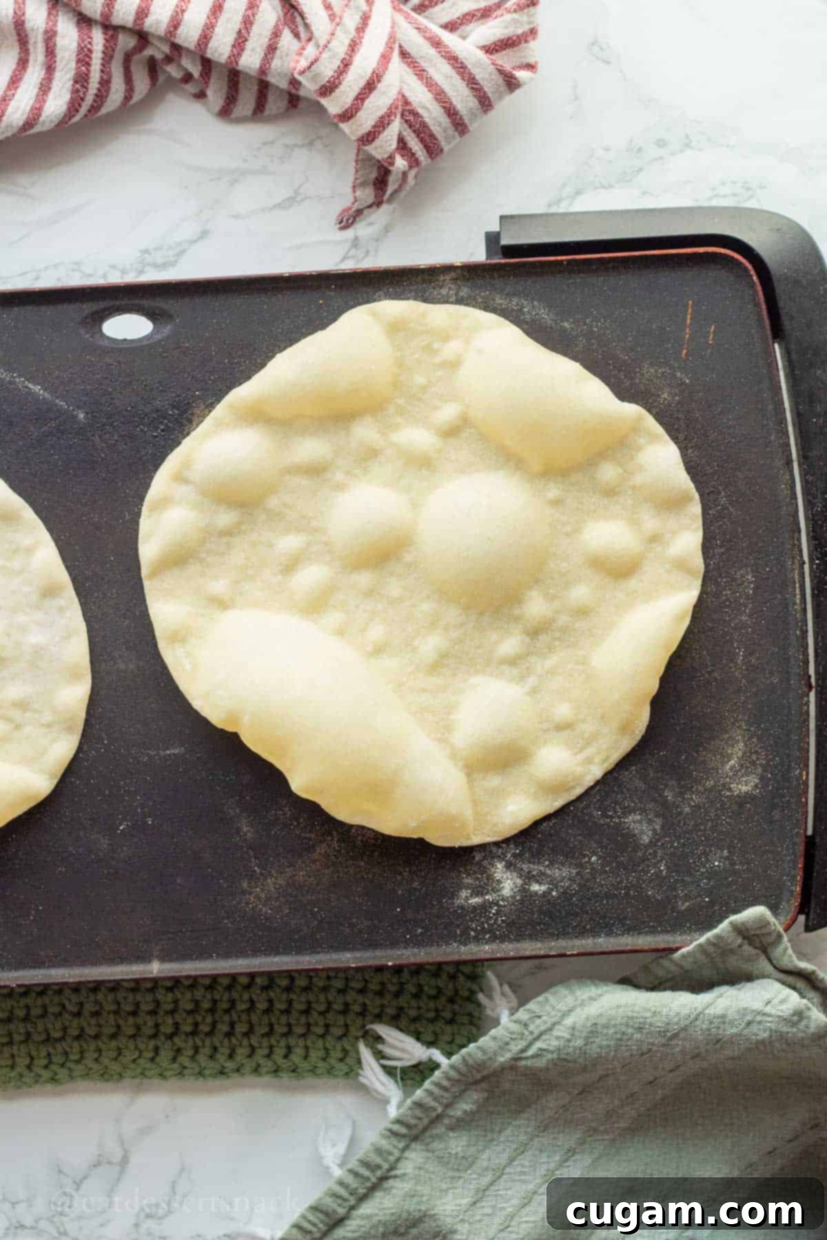 A sourdough discard tortilla cooking on a hot griddle, showing characteristic bubbles forming on its surface.