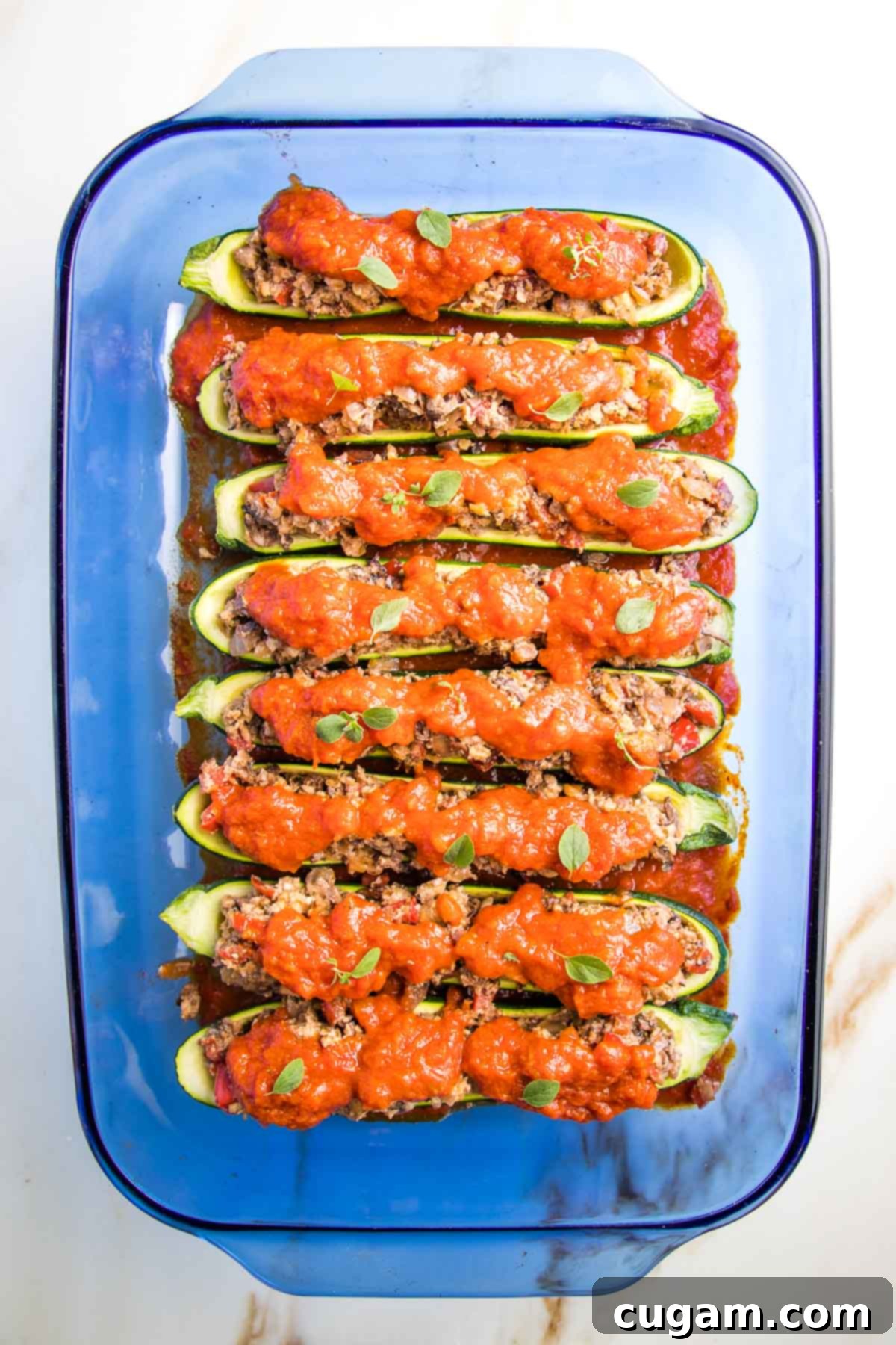 A baking dish containing zucchini boats already stuffed with the meaty vegan filling, beautifully topped with marinara sauce and sprinkled with vibrant fresh herbs, ready for the final bake.