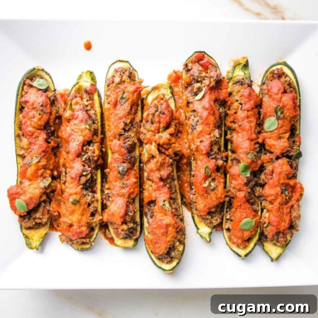 A beautifully arranged serving of zucchini boats, generously stuffed with a savory, meaty plant-based filling, topped with vibrant marinara sauce and fresh green herbs, presented as a delicious and wholesome meal.