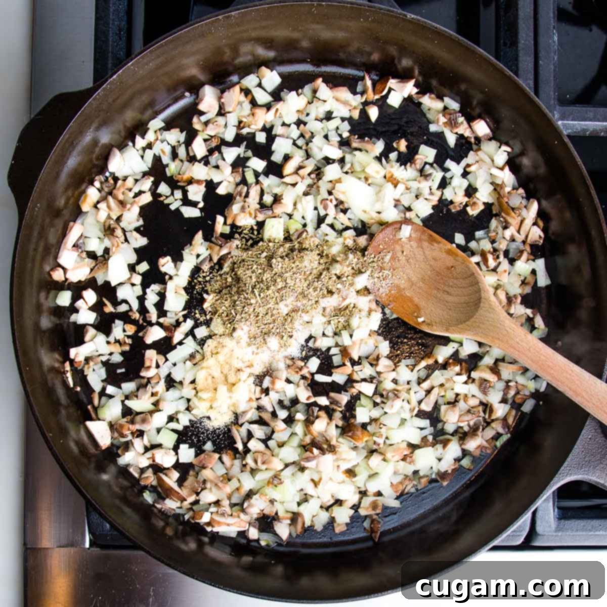 A cast iron skillet on a stovetop, filled with sautéing onions, finely diced mushrooms, and a variety of aromatic spices, creating a fragrant and flavorful base for the filling.