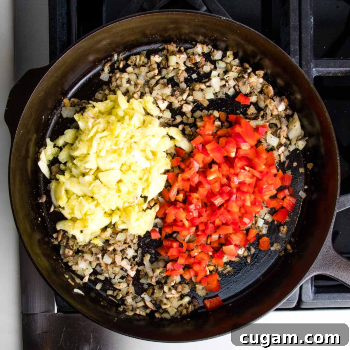 The cast iron skillet now contains the sautéed onions, mushrooms, and spices, with additional diced bell peppers and the roughly chopped zucchini pulp stirred in, continuing to cook and tenderize.