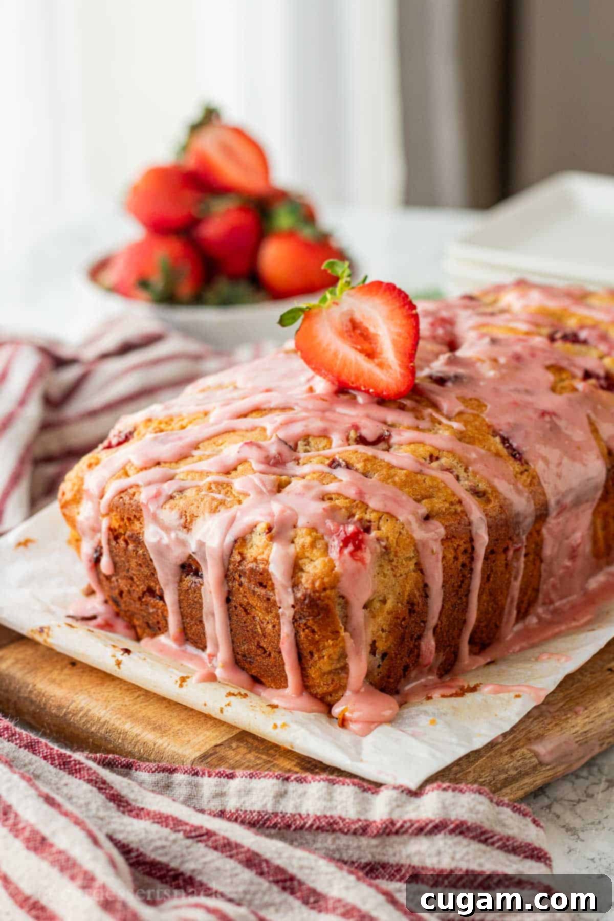 Baked loaf of strawberry banana bread with icing and strawberry on top, ready to be sliced and served.
