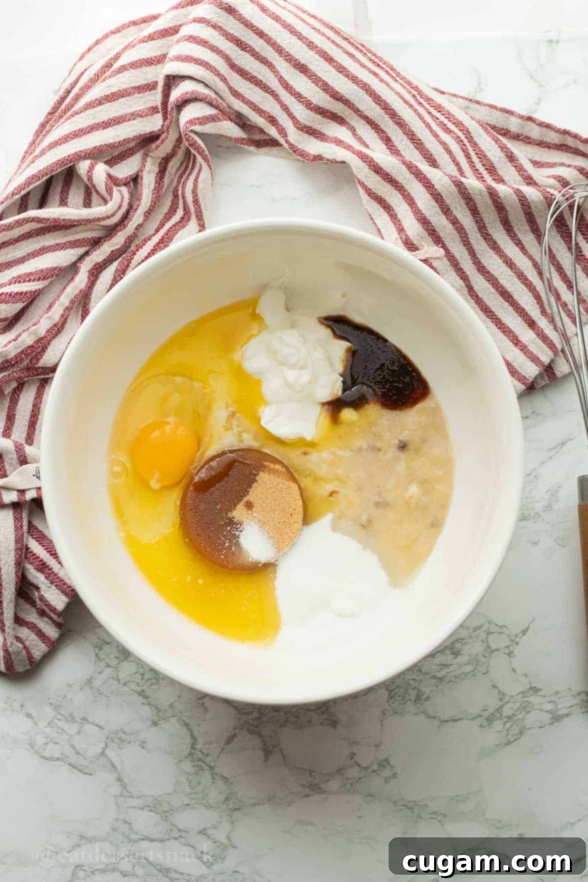 Brown sugar, egg, sour cream, vanilla, and mashed banana in a white mixing bowl, representing the wet ingredients for strawberry banana bread.
