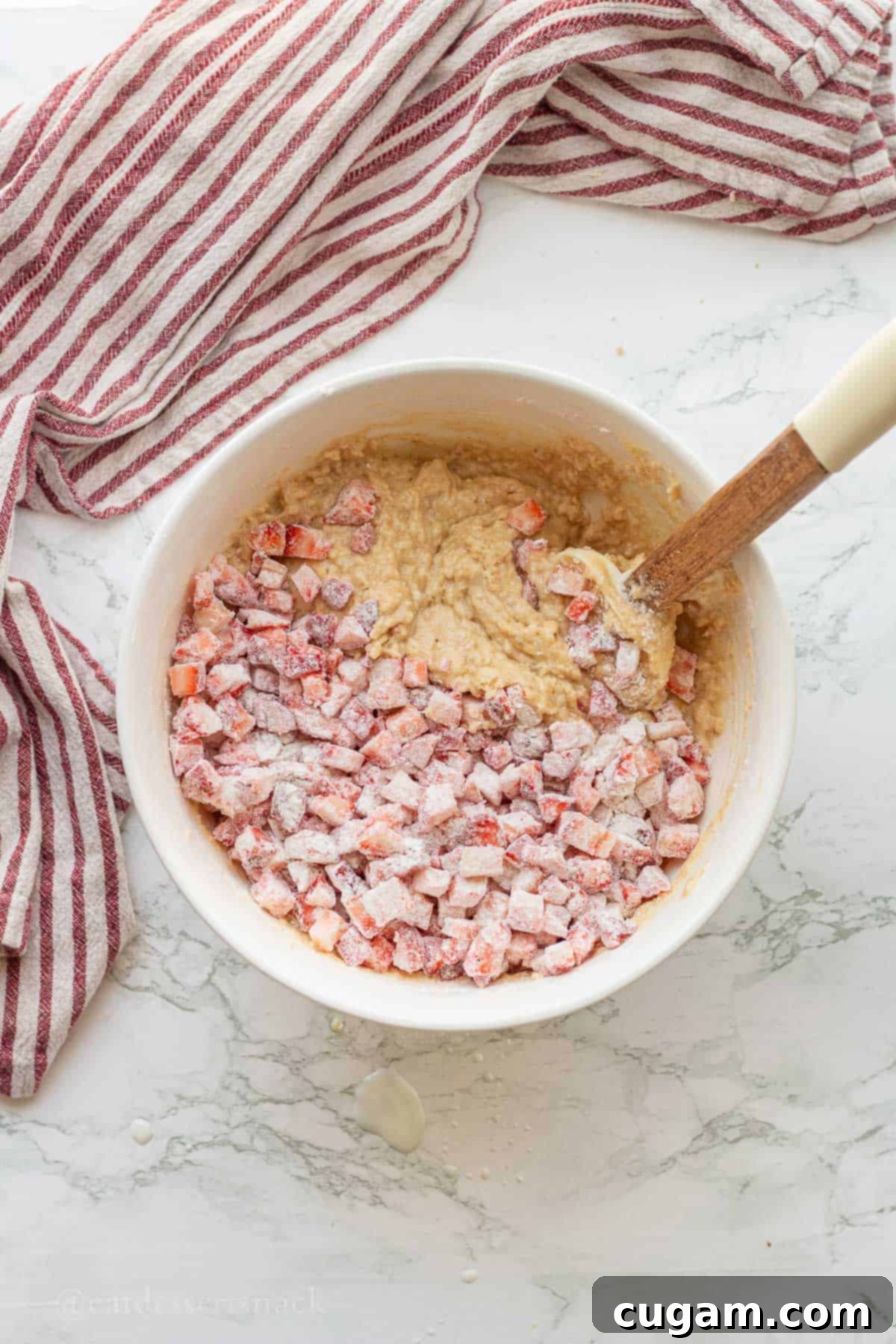 Flour-tossed diced strawberries being folded into the raw banana bread batter in a white mixing bowl.