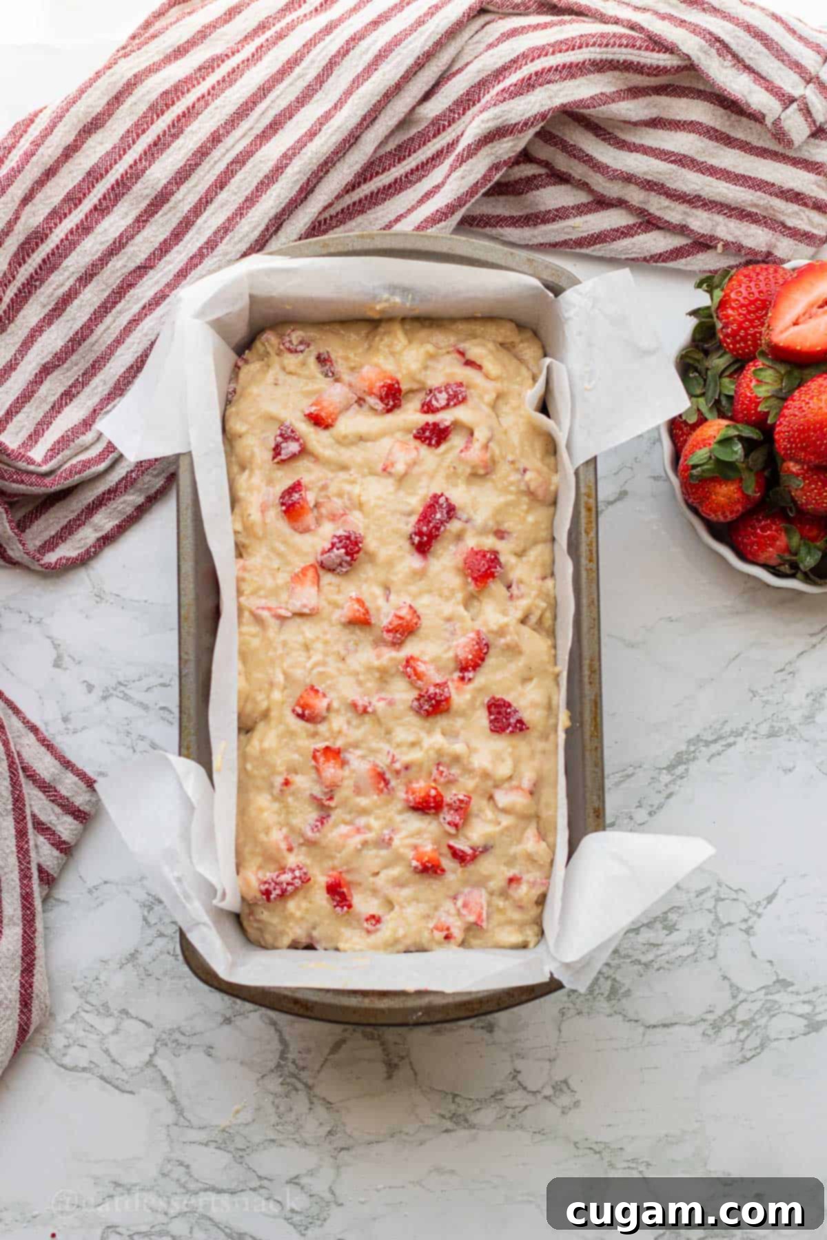 Raw strawberry banana bread batter poured into a greased loaf pan lined with parchment paper, ready for baking.