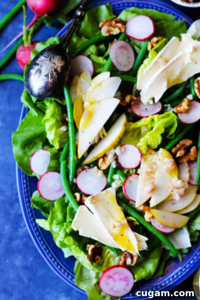 French Salad with Brie and Pears on a blue serving plate, showcasing fresh ingredients like lettuce, green beans, radishes, and walnuts.