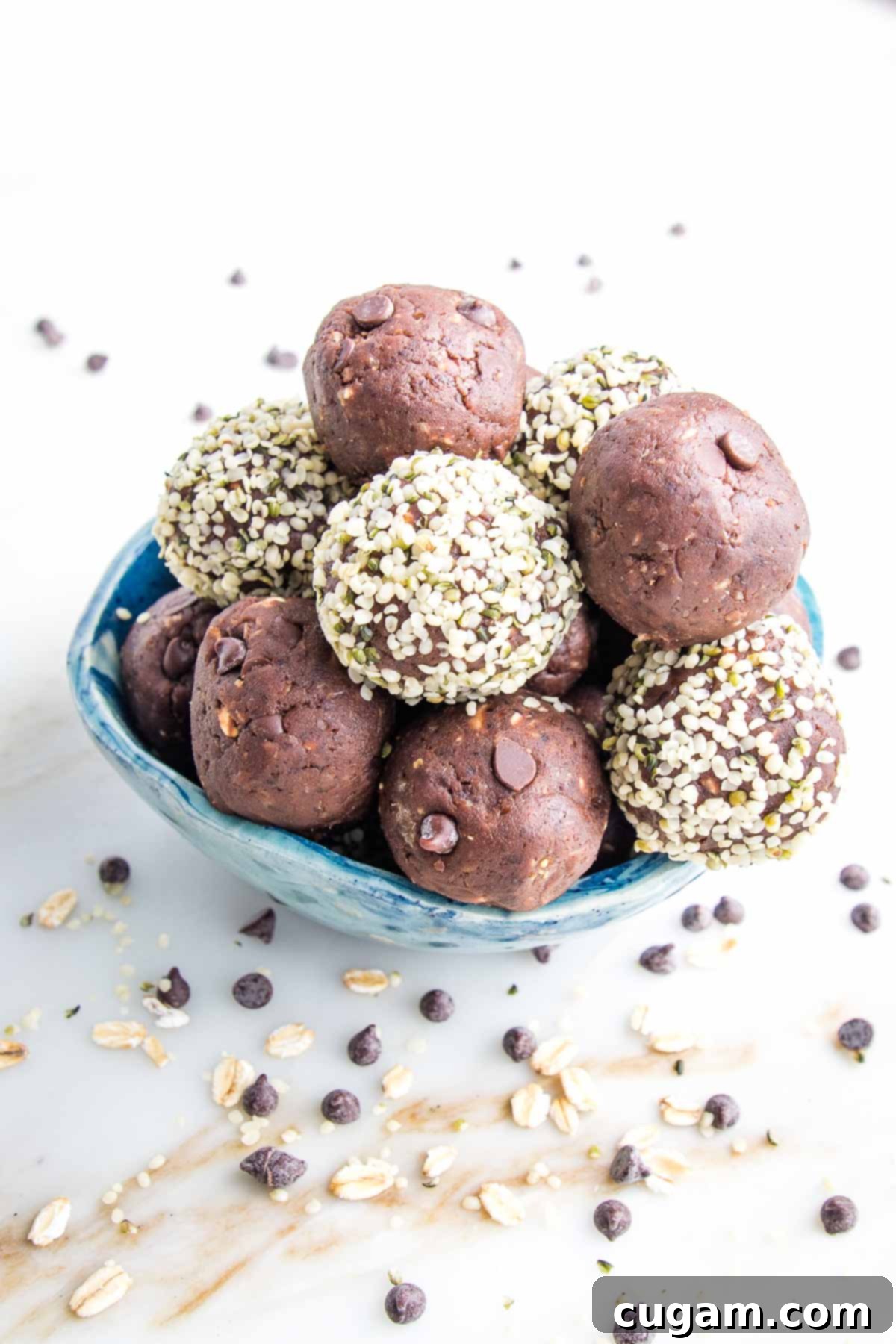 Small blue bowl filled with chocolate cookie dough bites, some have a hemp seed coating on the outside. The bowl is on a white marble countertop with mini chips sprinkled around.