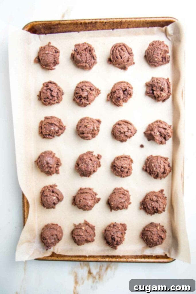 chocolate cookie dough balls scooped onto a rimmed baking tray lined with parchment paper