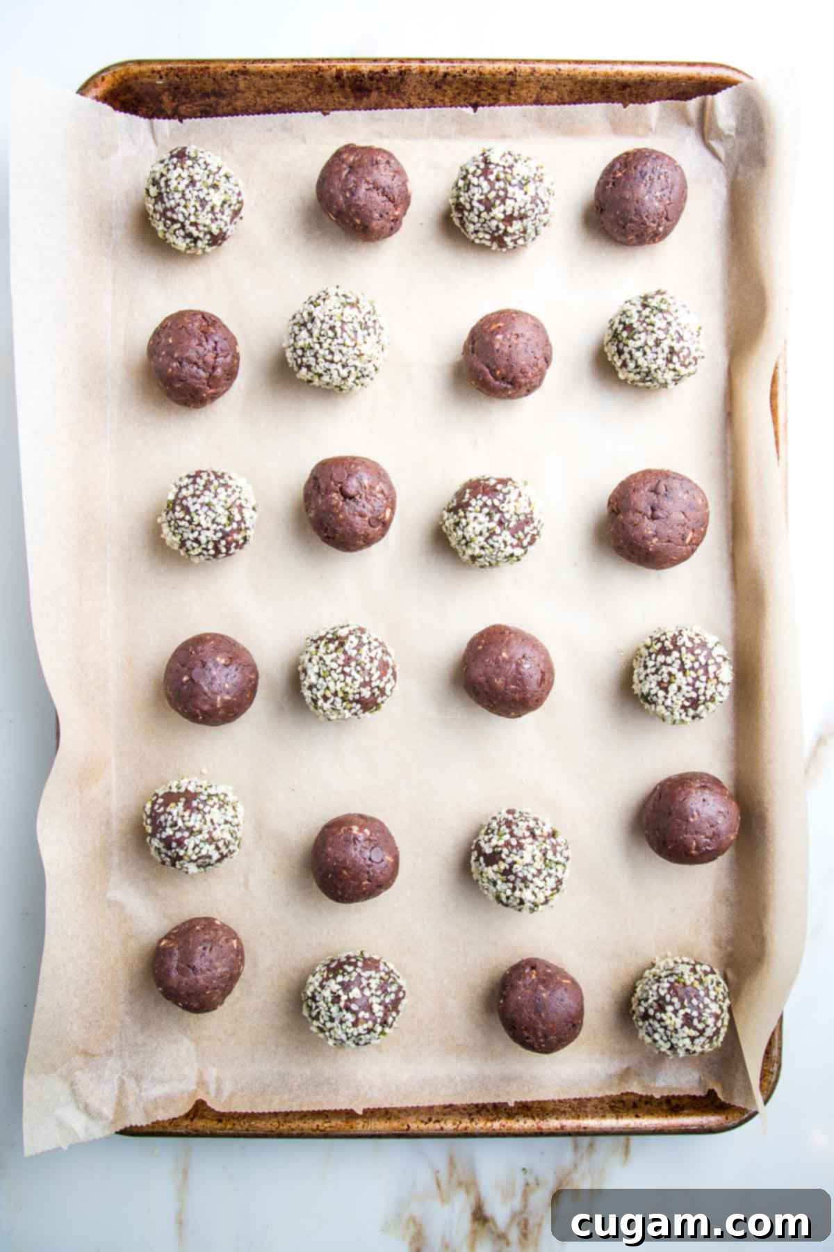Tray lined with unbleached parchment paper and filled with chocolate balls, some of them are rolled into hemp seeds.