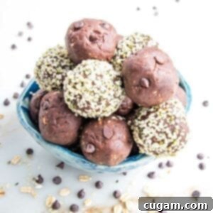 Small blue bowl filled with chocolate cookie dough balls. Some have a coating of hemp seeds on the outside. There are mini chocolate chips and bits of rolled oats scattered around the bowl on a white marble countertop.