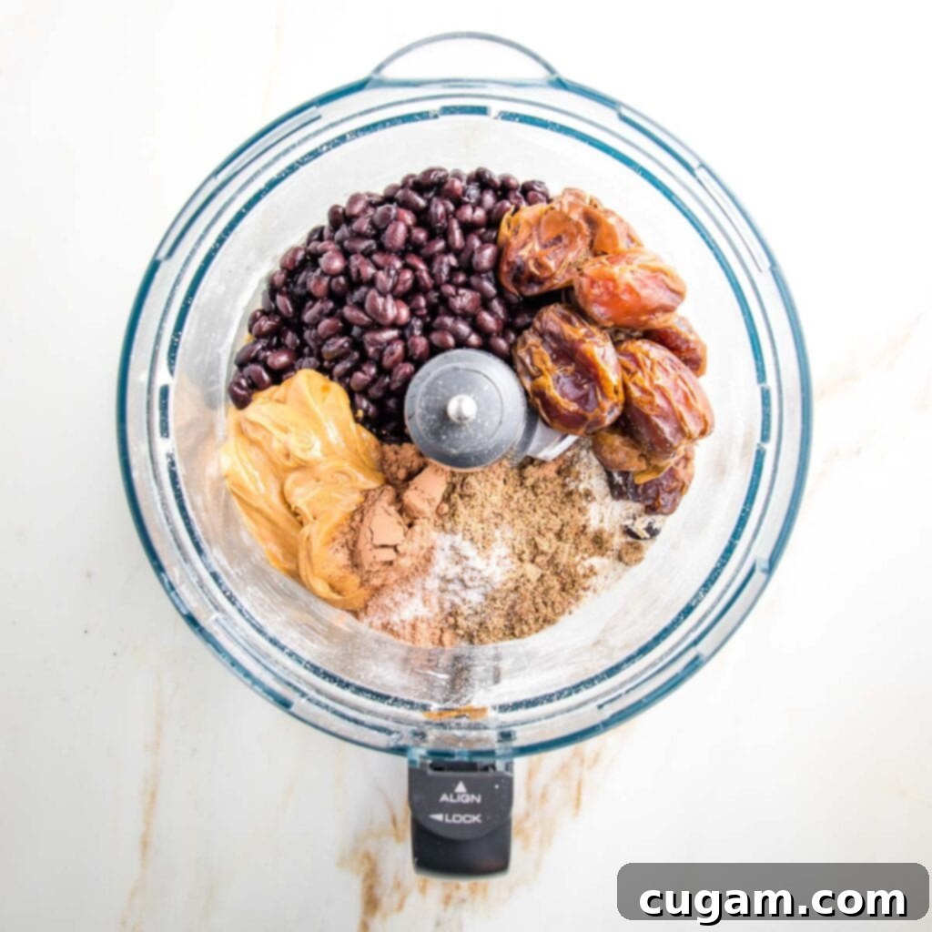 Food processor bowl filled with black beans, peanut butter, cacao powder, dates, ground flax and salt