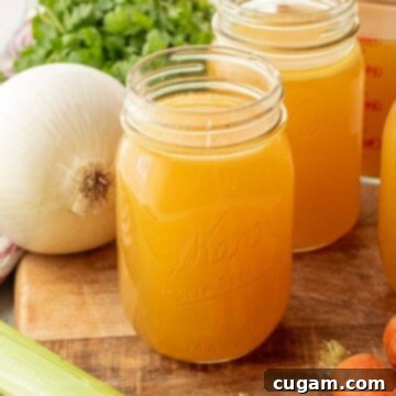 Chicken bone broth in jar on wood cutting board with fresh vegetables like carrots, celery, and onion.