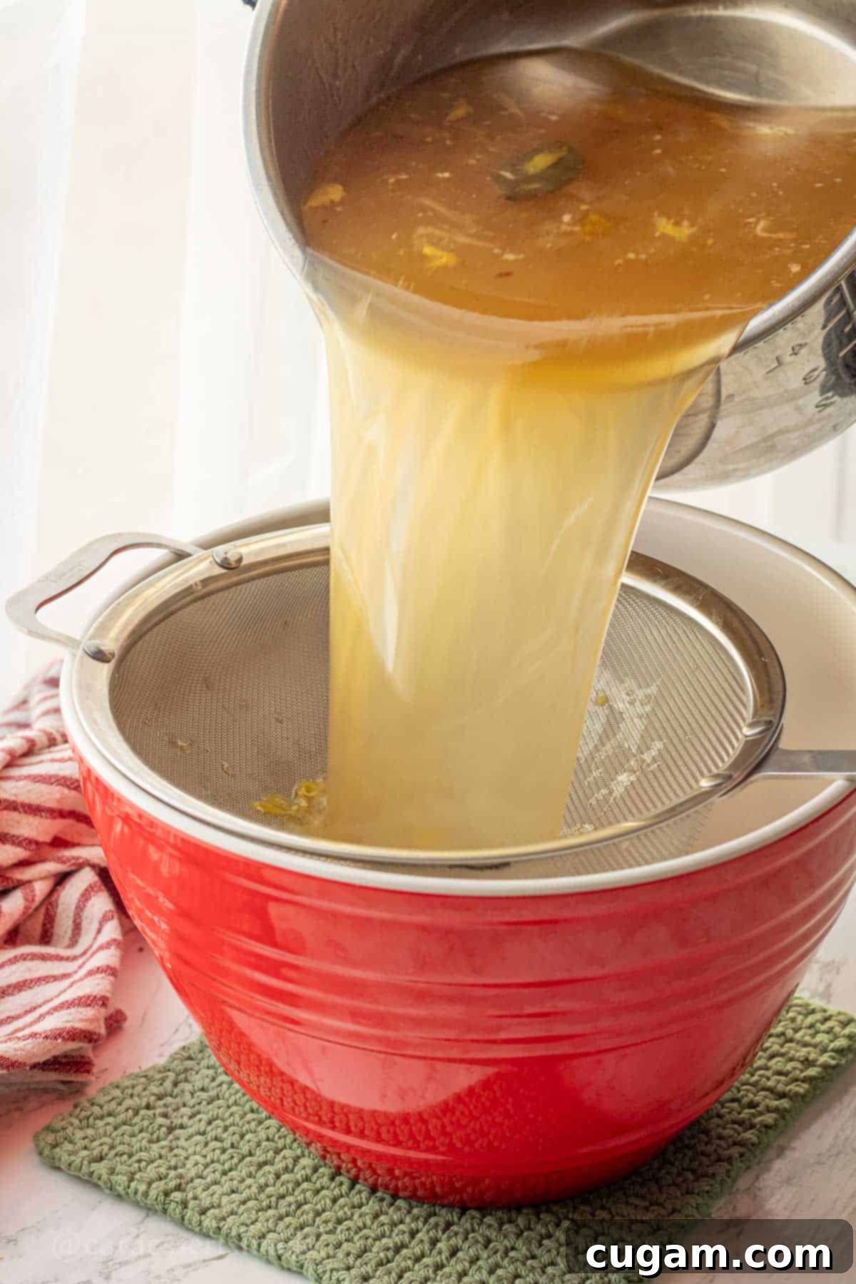 Pouring freshly made chicken bone broth through a mesh strainer into a large bowl.