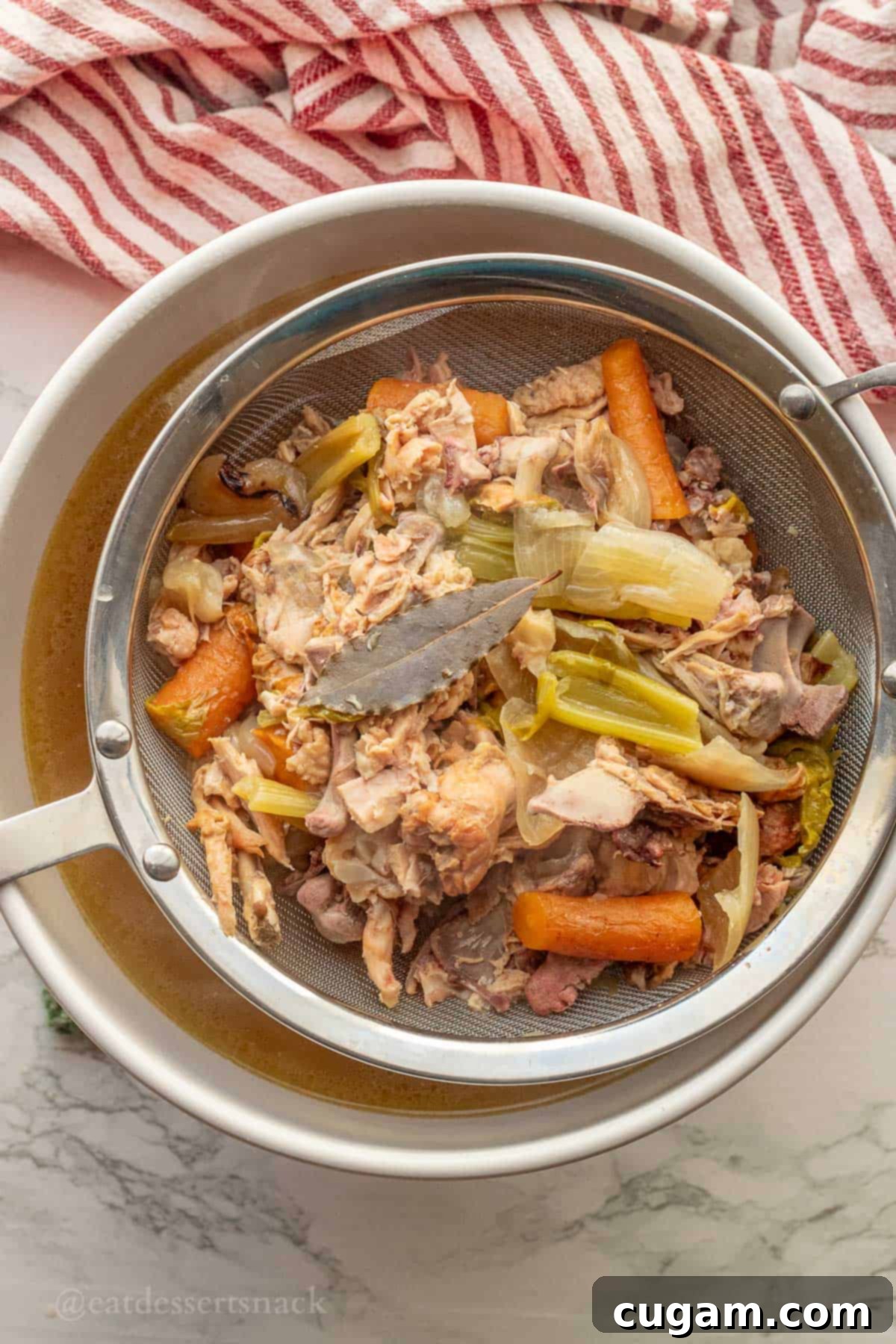 Cooked bones and vegetable scraps in a mesh strainer after the broth has been drained.