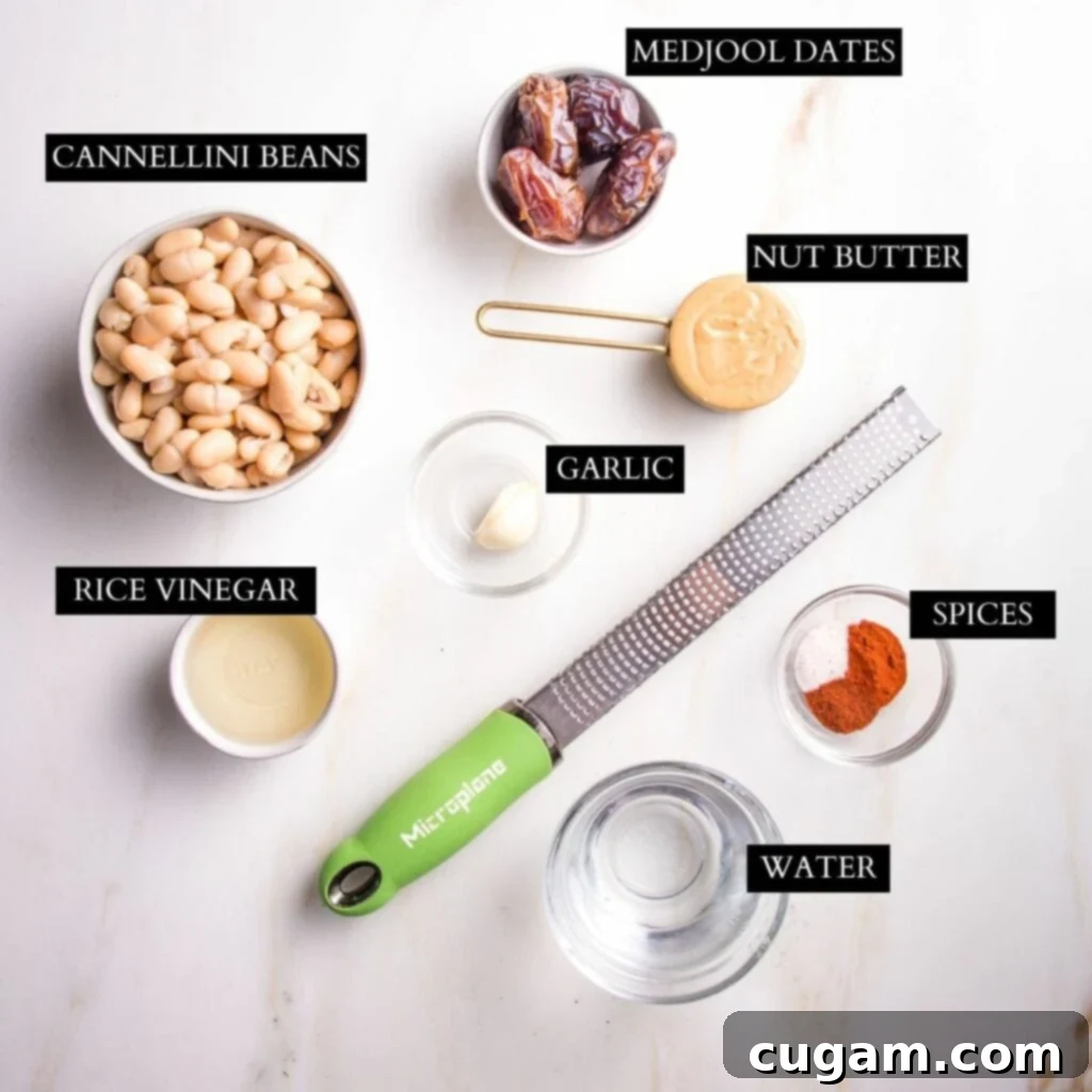Assorted ingredients for chipotle dressing on a white background, including a can of beans, dates, cashew butter, garlic, rice vinegar, and spices.