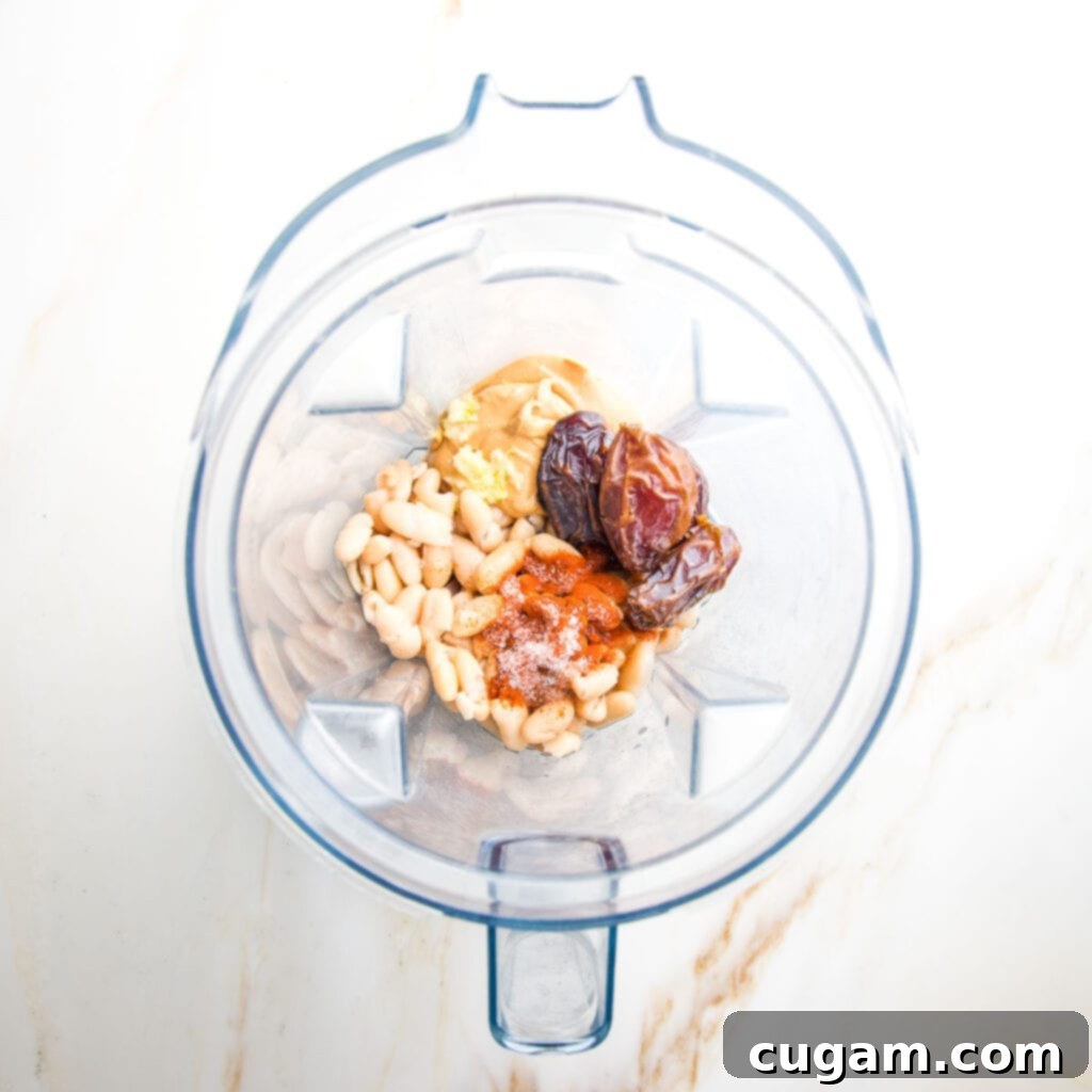 Blender pitcher filled with ingredients: white beans, dates, cashew butter, spices, garlic, vinegar.